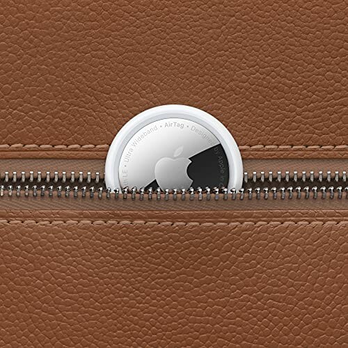 Apple AirTag partially visible in a brown leather bag zipper.