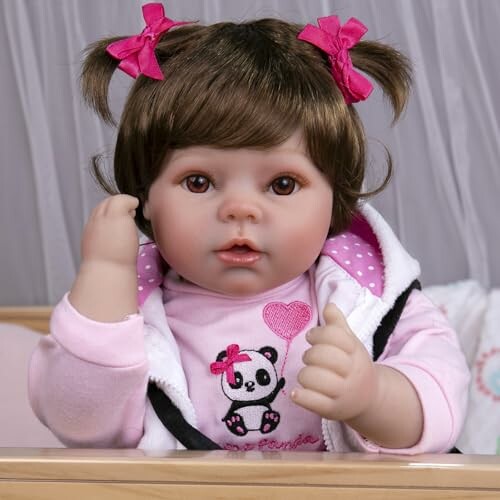 Realistic baby doll with pink bows in hair and panda shirt.