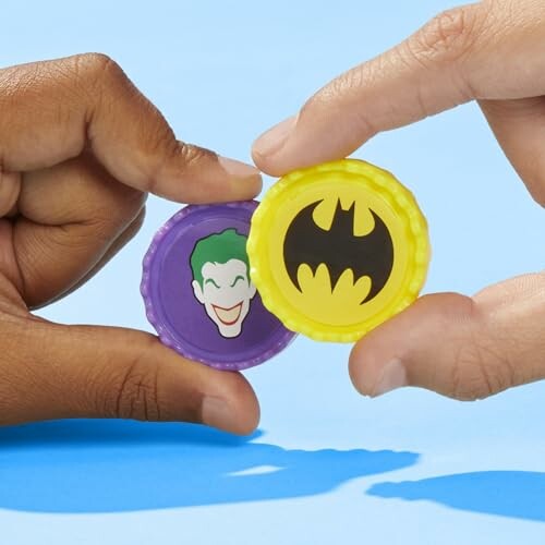 Hands holding Batman and Joker bottle caps.