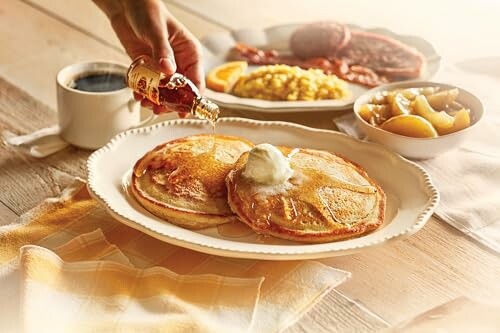 Pancakes with syrup and butter served with coffee, bacon, eggs, and fruit.