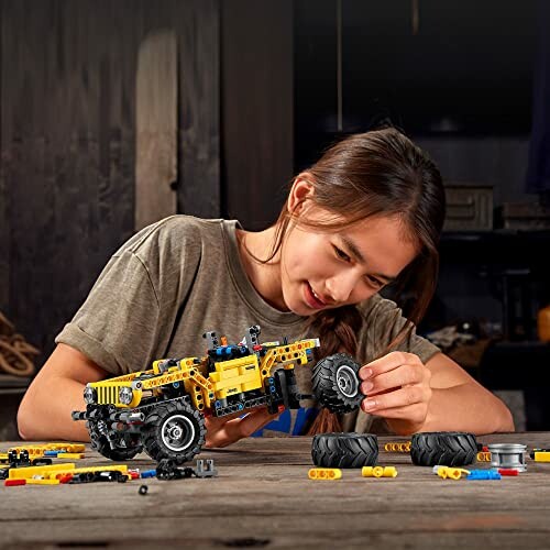 Child assembling a LEGO vehicle with yellow and black pieces.