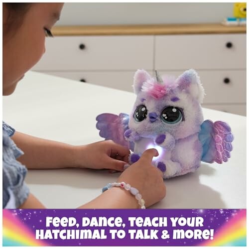 Child playing with a plush Hatchimal toy on a table.