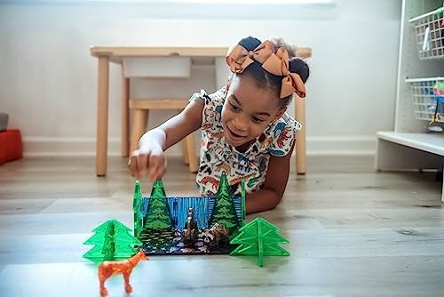 Child playing with toy figures and trees on the floor.