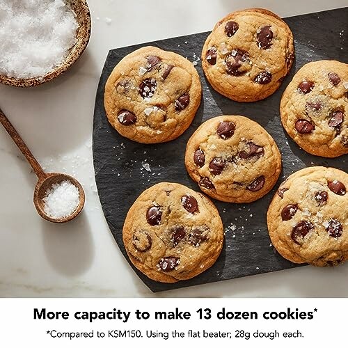 Six chocolate chip cookies on a slate with a bowl of salt.