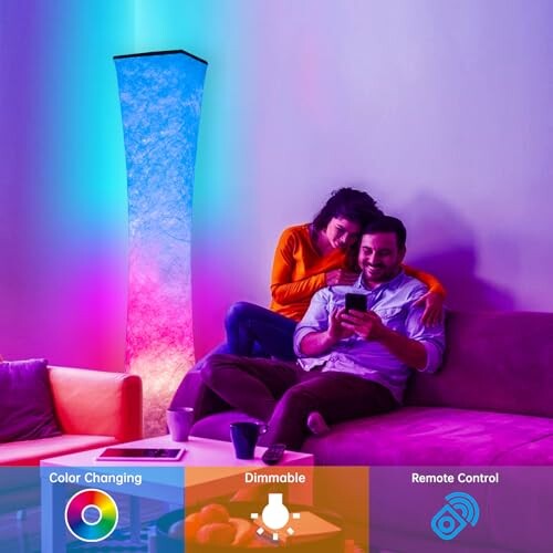 Couple sitting on a couch using a remote to control a color-changing floor lamp.