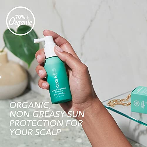 Person holding Coola organic scalp sunscreen spray.