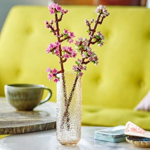 Decorative flowers in a textured vase on a table with a cup and book.