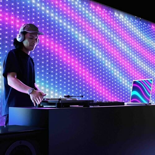 DJ performing with headphones and a laptop against a colorful LED backdrop.