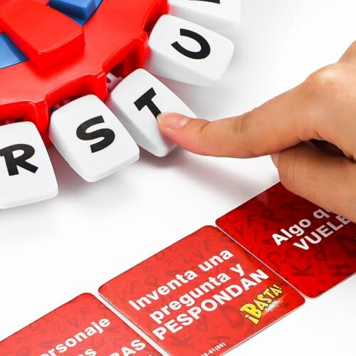 Finger pressing a letter button on a word game device next to red cards.