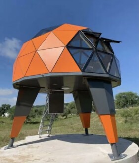 Modern geodesic dome structure with orange panels on elevated legs.