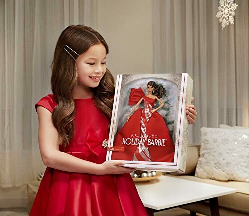 Girl holding a Holiday Barbie doll in red dress.