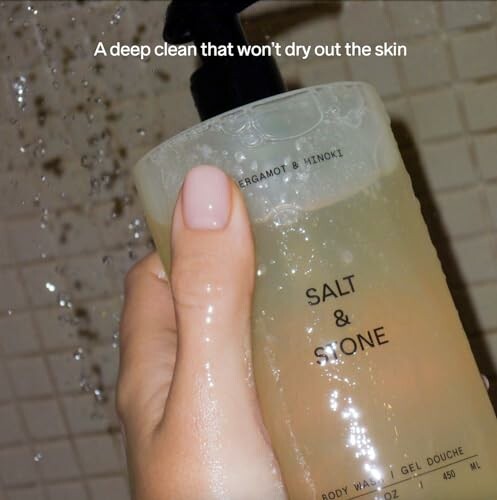 Hand holding a bottle of Salt & Stone body wash under running water