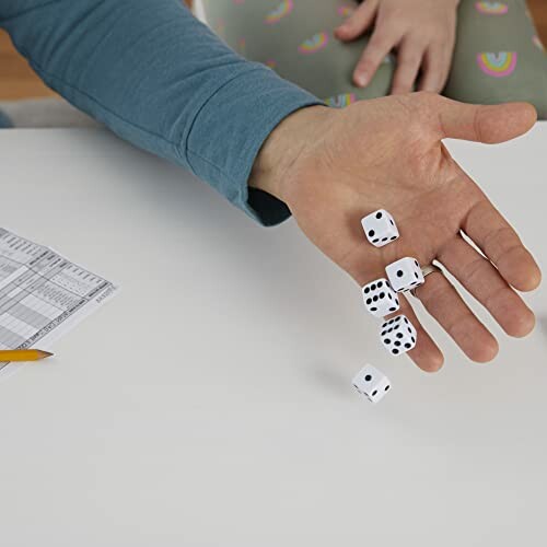 Hand rolling dice on a table with a paper and pencil nearby