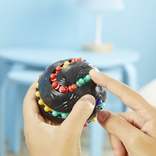 Hands holding a black puzzle ball with colorful beads.