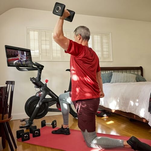 Person exercising on a stationary bike with a dumbbell in a bedroom.