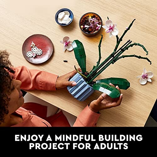 Person assembling a LEGO orchid model on a wooden table.