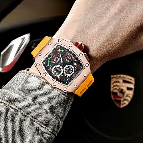 Luxury watch with yellow strap on wrist, car interior in background.