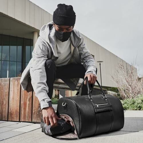 Man with a mask packing items into a black gym bag outdoors.