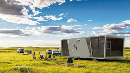 Modern camping trailer and chairs in open field with blue sky.