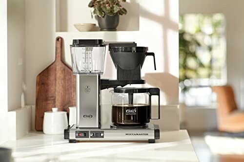 Modern coffee maker on kitchen counter with coffee pot and cutting board.