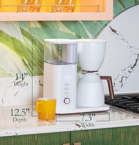 White coffee maker on kitchen counter with cup, measuring dimensions.