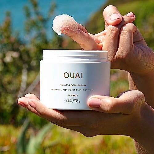 Person holding Ouai Scalp and Body Scrub outdoors.