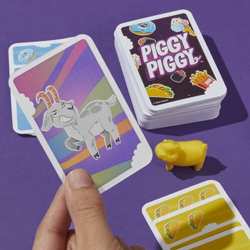 Person holding a card with a goat, surrounded by Piggy Piggy card game elements.