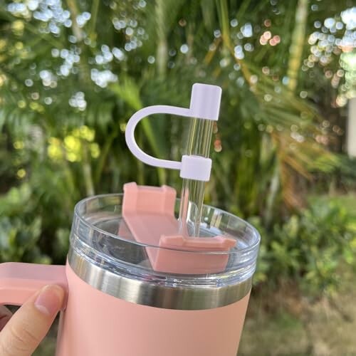 Pink tumbler with a straw against a blurred green background