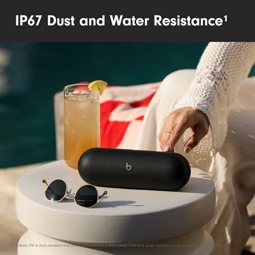 Portable speaker with IP67 dust and water resistance beside a drink and sunglasses.