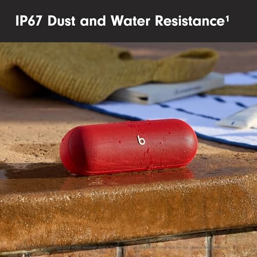 Red Bluetooth speaker with IP67 dust and water resistance on wet surface.