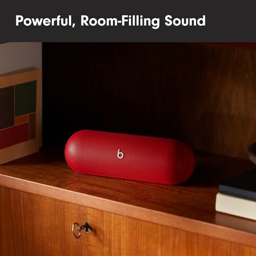 Red wireless speaker on a wooden shelf with books.