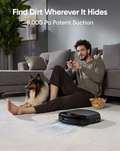 Man with remote control and dog near robot vacuum cleaner in living room.