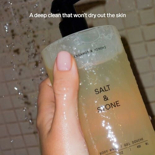 Hand holding Salt & Stone body wash bottle, shower background