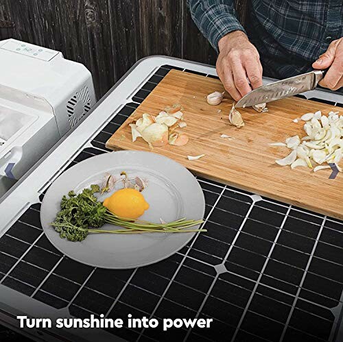 Person chopping onions on a solar panel with herbs and egg on a plate.