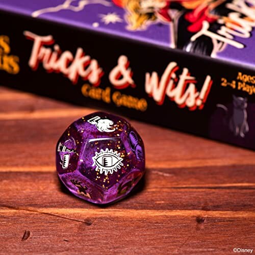 Purple dice on wooden table with Tricks & Wits card game.