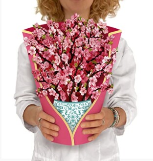 Person holding a cherry blossom bouquet in a decorative pink wrap.