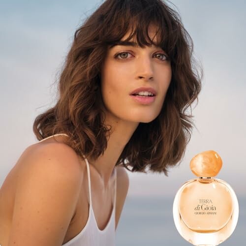 Woman with shoulder-length hair beside a perfume bottle.