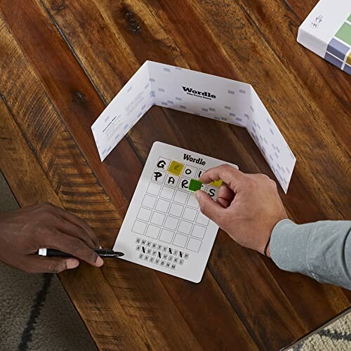 Two people playing a Wordle board game on a wooden table.